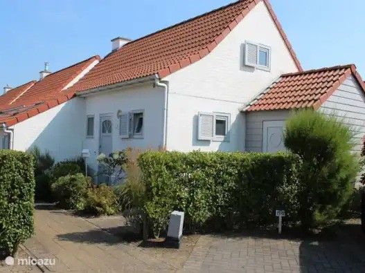 Charmant vakantiehuis Seaside Village, huisje 77, in Vosseslag bij De Haan aan de Belgische kust, met rode daken en groene heggen.