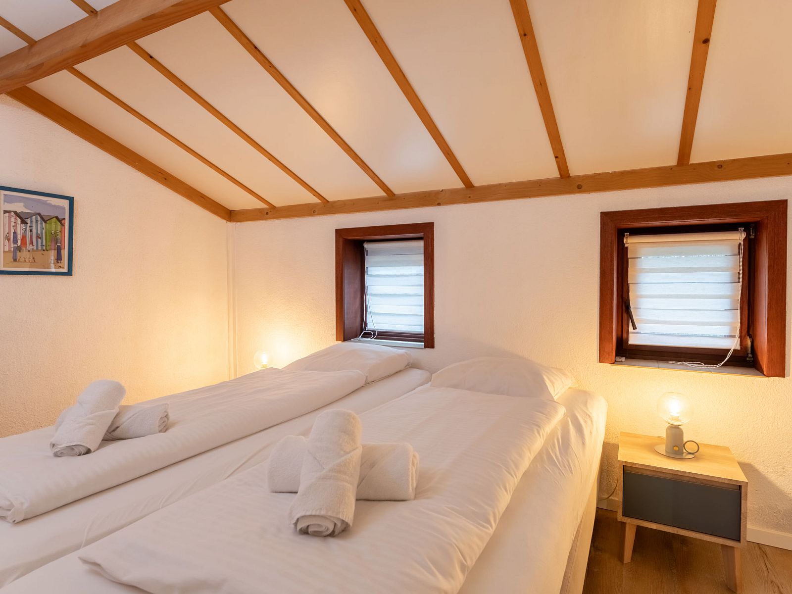 Gezellige slaapkamer in Vakantiehuis Strandhuis te Bredene, Belgische kust, met houten balkenplafond en knusse verlichting voor een ontspannen verblijf.