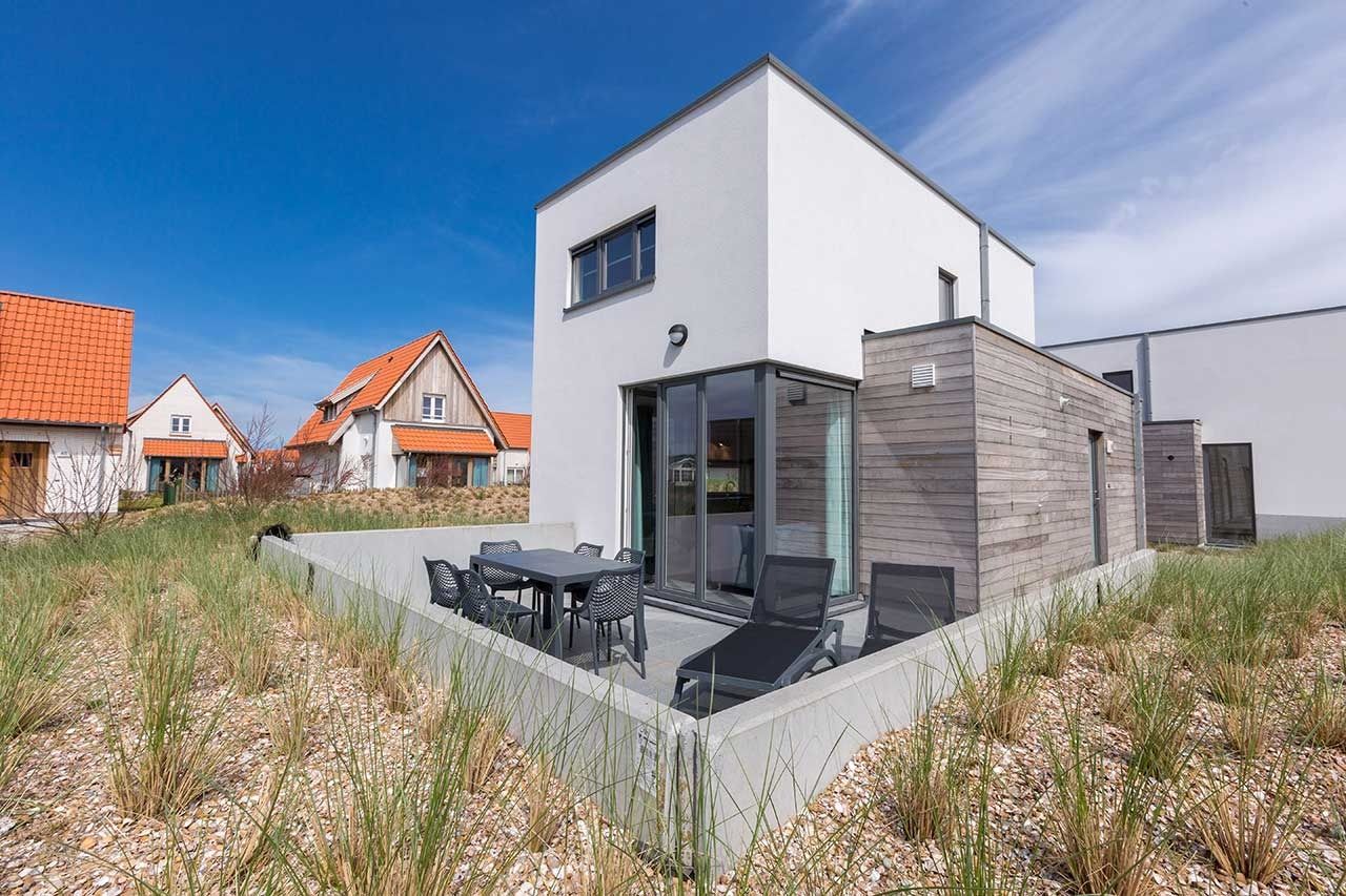 Vrijstaande woning in Bredene, Belgische kust: modern vakantiehuis met terras en ligstoelen, omringd door duinen en natuur.