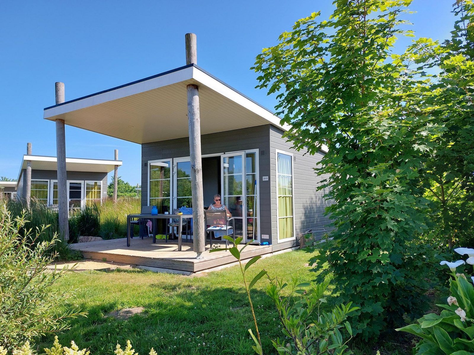 Comfort Lodge in Westende, Belgische kust, biedt een charmante vakantie-ervaring met een ruime veranda en groene omgeving.