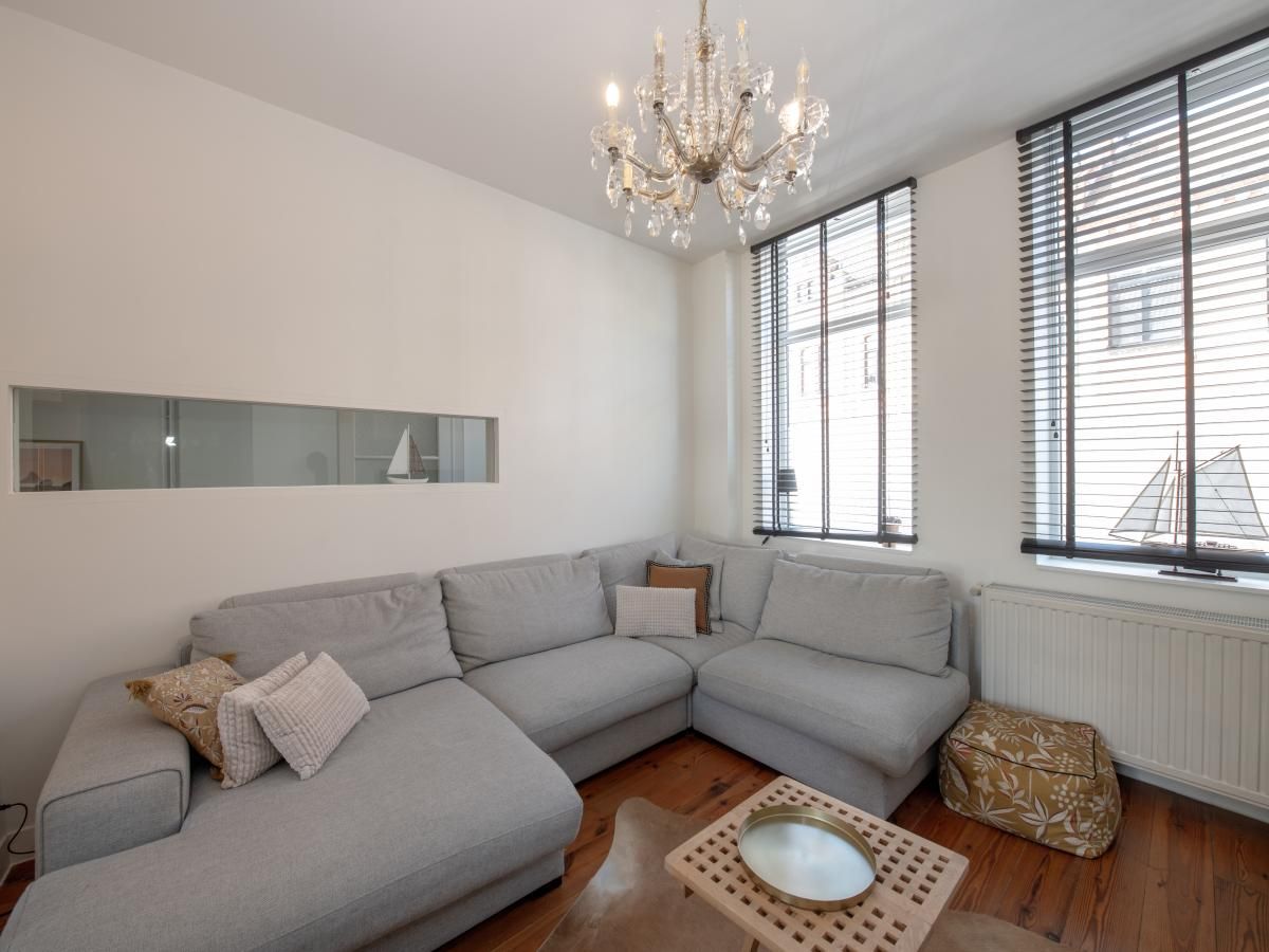 Stijlvolle woonkamer in vakantiehuis Notre Dame, Nieuwpoort, Belgische kust. Comfortabele hoekbank en elegante kroonluchter voor een ontspannen verblijf.