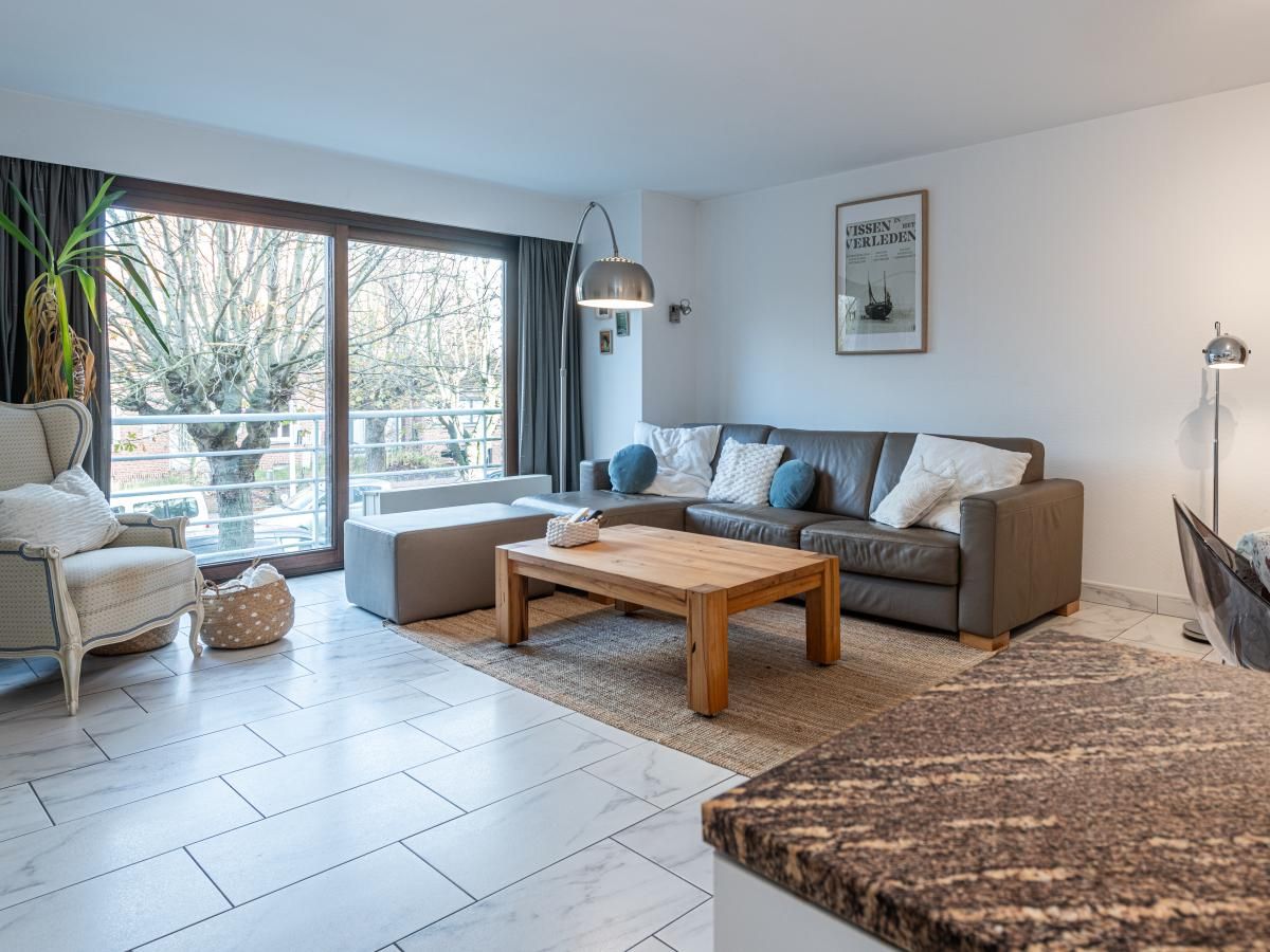 Gezellige woonkamer in vakantiehuis Reigersnest, Nieuwpoort, Belgische kust, met comfortabele zithoek en uitzicht op groene omgeving.
