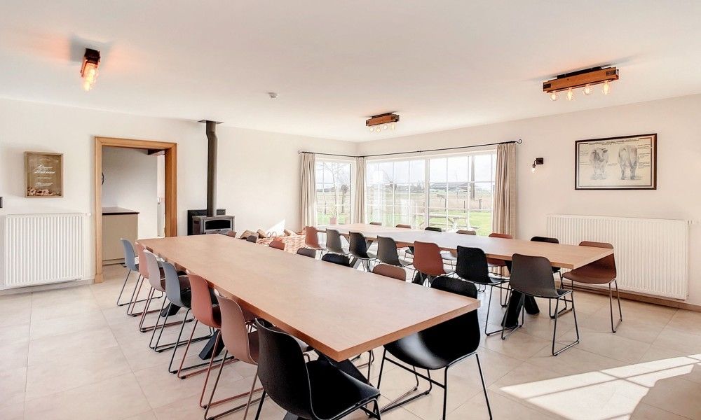 Eetkamer met lange tafels in Hoeve Langhof vakantiehuis, De Haan, ideaal voor groepsdiners.