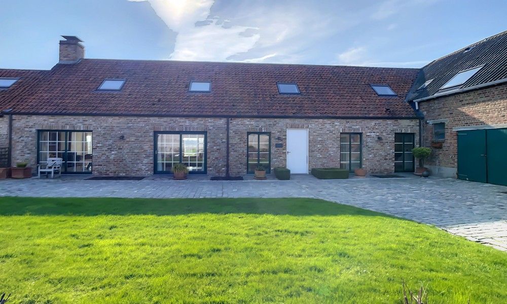 Hoeve Langhof vakantiehuis in De Haan, Belgie, met groene tuin en traditionele architectuur.