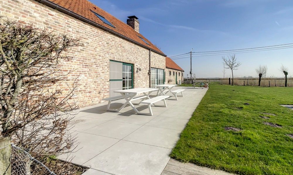 Veranda met zitgelegenheid bij Hoeve Langhof vakantiehuis, De Haan, omringd door groen.