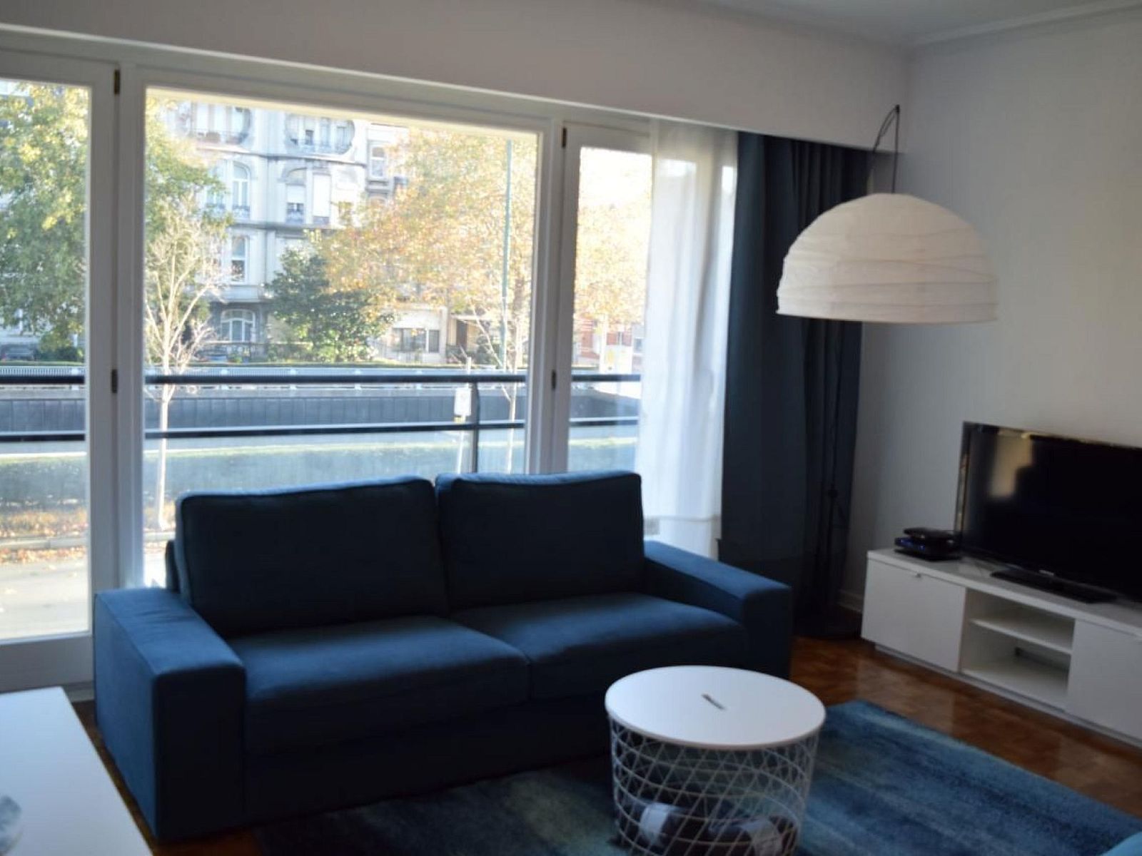 Gezellige woonkamer in Appartement in Woluwe-Saint-Lambert, Brussel met uitzicht op de stad, comfortabele bank en moderne inrichting.