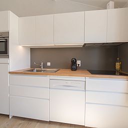 Moderne Kueche im Ferienhaus Duinenhuisje 25 mit schlichten weissen Schraenken, gelegen in De Haan, Westflandern, ideal fuer einen entspannten Aufenthalt.