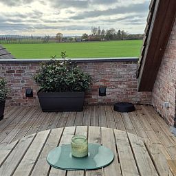 Geniessen Sie die Aussicht auf die gruene Landschaft von der Terrasse des Ferienhauses in PROVEN, Westflandern, Belgien.