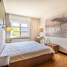 Sfeervolle slaapkamer in Juvamy gelijkvloers vakantiehuis, Koksijde, Belgie, met rustgevend interieur en grote ramen voor natuurlijk licht.