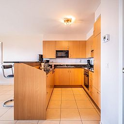Moderne keuken in vakantiehuis Paco vierde, Koksijde, West-Vlaanderen. Ruime binnenruimte met houten kasten en tegelvloer.