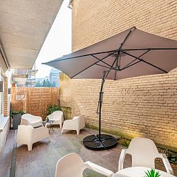 Ontspan op het terras van vakantiehuis Bon Plan in Koksijde, West-Vlaanderen, met moderne zitjes en een grote parasol voor schaduw.