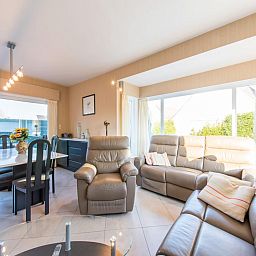 Gezellige woonkamer in vakantiehuis Mallory, Koksijde, met comfortabele banken en veel natuurlijk licht, ideaal voor ontspanning in West-Vlaanderen.