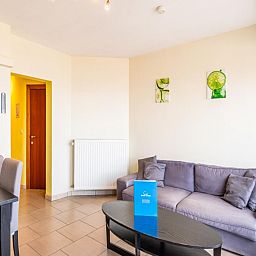 Gezellige woonkamer in vakantiehuis Vitelli, Koksijde, West-Vlaanderen. Comfortabele zithoek met moderne inrichting en kunst aan de muur.