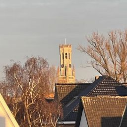 Blick auf den historischen Turm von Flat Memling in Sint-Andries, Westflandern, Belgien, umgeben von baumbestandenen Daechern.