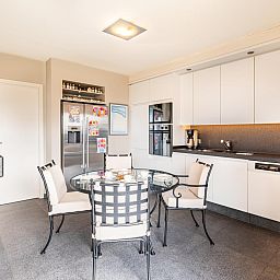 Moderne Kueche im Ferienhaus LaRoyale, De Panne, Westflandern, mit stilvollem Essbereich und schlichten weissen Schraenken.