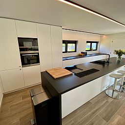 Moderne Kueche im Ferienhaus Petunias Deluxe, Sint-Idesbald, Westflandern. Luxurioeses Interieur mit Insel und glatter Oberflaeche.