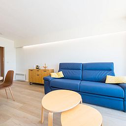 Modernes Wohnzimmer im Ferienhaus Reno - 0701 in Middelkerke, Westflandern mit bequemem blauen Sofa und Holzmoebeln.
