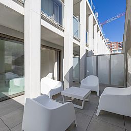 Moderne Veranda des Ferienhauses Omnia 7 - 0103 + Park. 5 in Middelkerke, Westflandern, Belgien, mit weissen Stuehlen und einem kleinen Tisch.