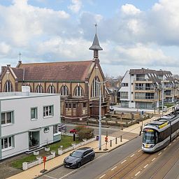 Blick vom Ferienhaus "Harmony - 0301" in Middelkerke, Westflandern, mit der Kirche und der Kuestenstrassenbahn in der Strasse.