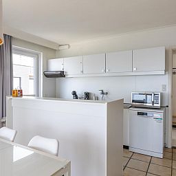 Moderne Kueche im Ferienhaus Kwintebank - 0904 in Middelkerke, Westflandern, Belgien, mit schlichten weissen Schraenken und Essbereich.