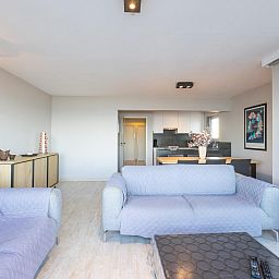 Helles Wohnzimmer im Ferienhaus Dunekant, Middelkerke, mit bequemen Sofas und moderner Kueche in Westflandern, Belgien.