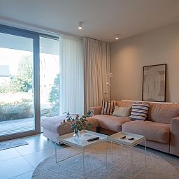 Gezellige woonkamer van West Bay vakantiehuis in Westende, West-Vlaanderen met comfortabele bank en uitzicht op de tuin.