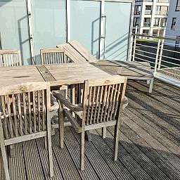 Zonnig terras van Appartement Cocoon in Bredene, West-Vlaanderen, Belgie, met houten tuinmeubilair en uitzicht op de moderne omgeving.