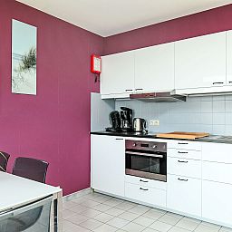 Moderne Kueche im Apartment Studio 604, Bredene, Westflandern, Belgien, mit stilvoller lila Wand und voll ausgestatteter Einrichtung.