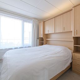 Schlafzimmer des Apartments Casa Bunck in Bredene, Westflandern, mit einem bequemen Doppelbett und natuerlichem Licht durch grosse Fenster.