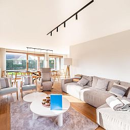 Helles Wohnzimmer des Ferienhauses "Pure Relax" in Oostduinkerke, Belgien, mit gemuetlicher Sitzecke und Blick auf den Garten.