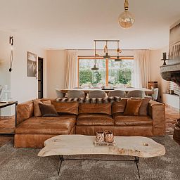Stijlvolle woonkamer van Villa Noortem, een vakantiehuis in Maldegem, Oost-Vlaanderen, met luxe leren bank en sfeervolle open haard.