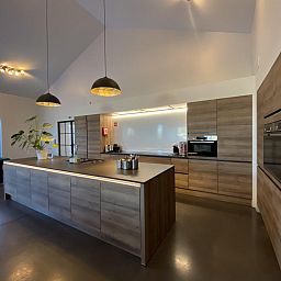 Moderne Kueche in der Villa Mareon, einem Ferienhaus in Maarkedal, Ostflandern, mit eleganten Holzoberflaechen und grosszuegiger Raumaufteilung.