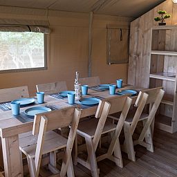 Gemuetlicher Essbereich im Safari-Zelt, einer Glamping-Lodge in Brecht, Antwerpen, Belgien, mit Holztisch und Stuehlen fuer einen gemuetlichen Aufenthalt.