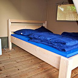 Gemuetliches Schlafzimmer im Safari-Zelt, einer Glamping-Lodge in Brecht, Antwerpen, Belgien, mit bequemem Holzbett und natuerlichem Licht.