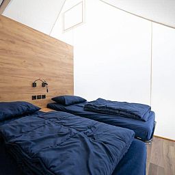 Bedroom in Kiezel Lodge XL, a glamping lodge in Mol, Antwerp, with comfortable beds and a modern wooden finish.