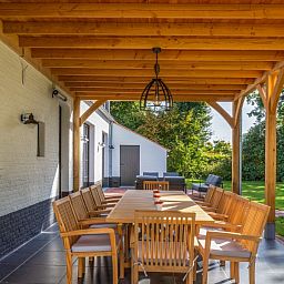 Ueberdachte Terrasse des Ferienhauses Mushoeve in Zoersel, Antwerpen, mit Esstisch aus Holz und Gartenblick.