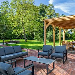 Mushoeve-Ferienhaus in Zoersel, Antwerpen mit gemuetlicher Sitzecke auf der Terrasse und gruenem Garten.