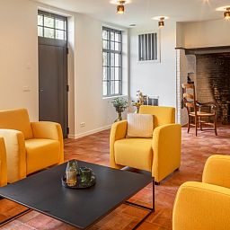 Gemuetliches Wohnzimmer von Mushoeve in Zoersel, Antwerpen mit Kamin und bequemen gelben Stuehlen.