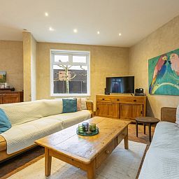 Gezellige woonkamer van vakantiehuis De Morgenstond in Baarle-Hertog, Antwerpen, met comfortabele banken en kleurrijke kunst aan de muur.