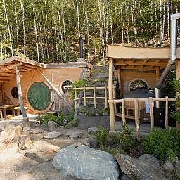 Hobbit House 1 in Neeroeteren, Limburg, Belgie, een uniek vakantiehuis met houten veranda, omgeven door groene natuur en rustieke charme.