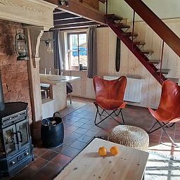 Gemuetliches Wohnzimmer im Chalet Pont du Waud in Waimes, Ardennen, Belgien, mit Holzofen und rustikaler Einrichtung fuer einen gemuetlichen Urlaub.