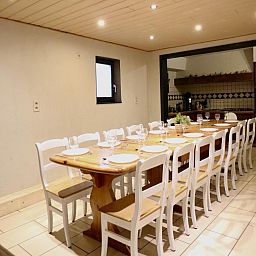 Ruime eetkamer van vakantiehuis Annexe in Sourbrodt, Ardennen, Belgie met lange houten tafel en moderne keuken in de achtergrond.