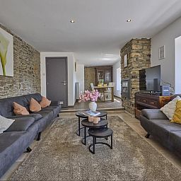 Gemuetliches Wohnzimmer im Ferienhaus "La Ferme" in Lierneux, Ardennen, mit bequemen Sofas und rustikalen Steinwaenden in Belgien.