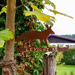 Das Ferienhaus in Kuechelscheid in den Ardennen, Belgien, bietet einen charmanten Aussenbereich mit einem gruenen Garten und einer rustikalen Holzfassade.