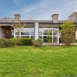 Buitenzijde van Village l'Eau d'Heure 12-persoons bungalow in Froidchapelle, Henegouwen, omgeven door groen en rustieke architectuur.