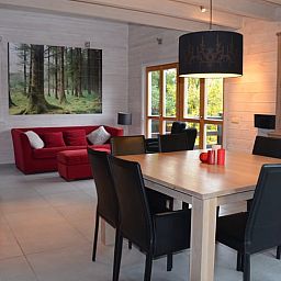 Gemuetlicher Innenbereich des Ferienhauses in Heure, Ardennen, Belgien mit grossem Esstisch und Blick auf die Natur.