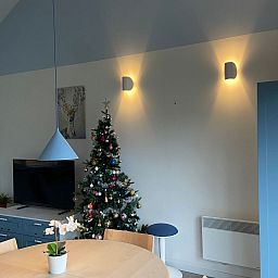 Gemuetliches Wohnzimmer im Ferienhaus Modernes Chalet in Heure, Ardennen, mit stimmungsvoller Weihnachtsdekoration und moderner Beleuchtung.