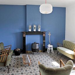 Stilvolles Wohnzimmer im Ferienhaus in Aublain in den belgischen Ardennen mit Vintage-Moebeln und einer blauen Akzentwand.