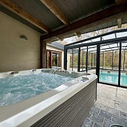 Ontspan in de luxe jacuzzi van Ry de Belle Rose, een vakantiehuis in Grupont, Ardennen, met uitzicht op het binnenzwembad en de omliggende natuur.