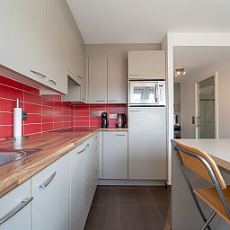 Modern kitchen in Apartment Ter Duyne, Bredene on the Belgian coast, with red tiles and sleek decor for a comfortable stay.